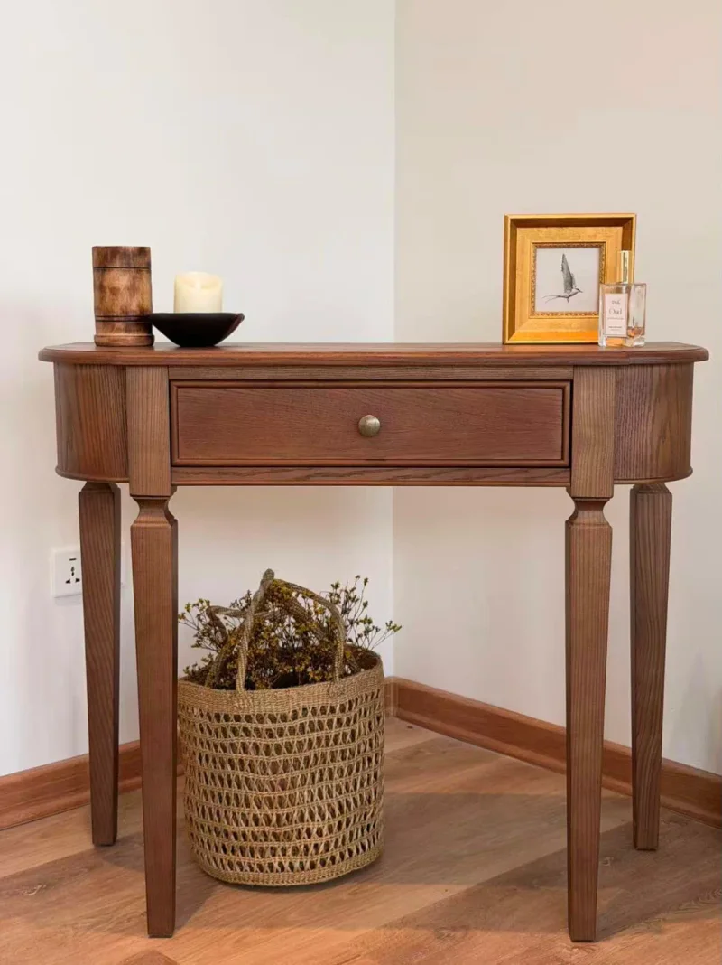 Rounded timber console with a drawer, styled with a small bird picture and candle, with a basket beneath.