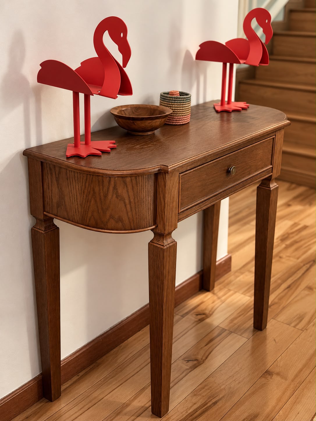 Wooden console with red flamingo ornaments beside a staircase