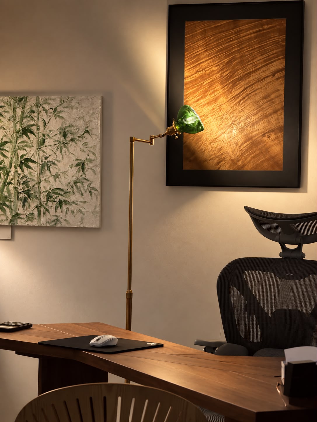 Green-shaded floor lamp beside a wooden desk and framed artwork
